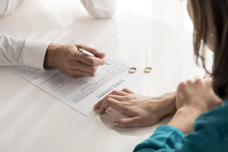 Person signing divorce paperwork with two wedding rings set on the table between the couple