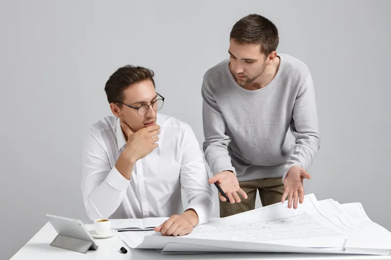 Two men studying a set of blueprints spread across a white desk