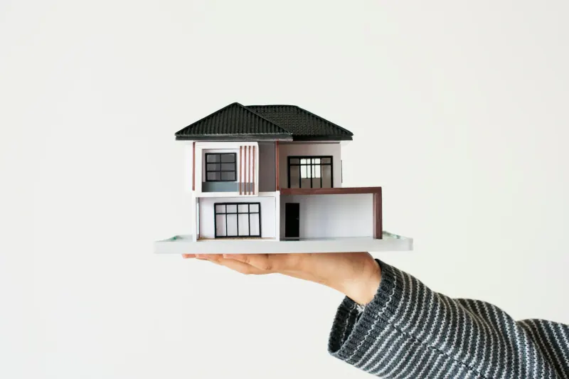 Hand holding a small two-story model house against a white background