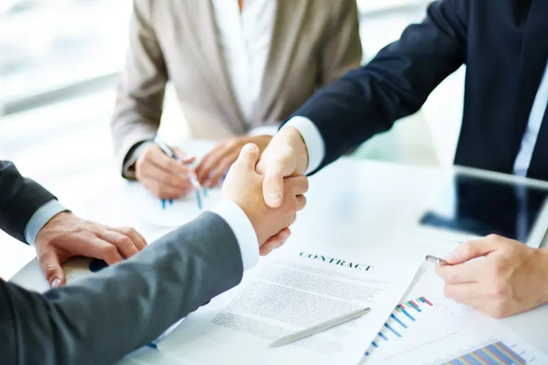 Business professionals shaking hands across a meeting table over a signed contract