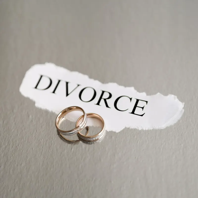 Two wedding rings resting on a torn strip of paper printed with the word “Divorce”