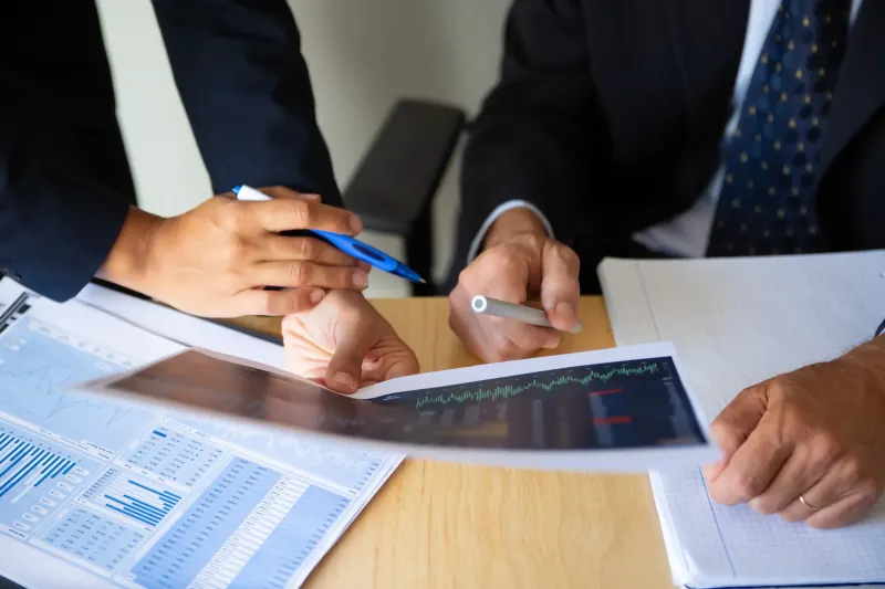 Two professionals reviewing printed financial charts and reports at a desk