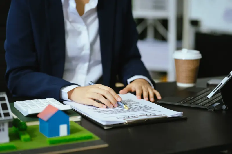Real estate professional reviewing a property document beside a calculator and a small model house